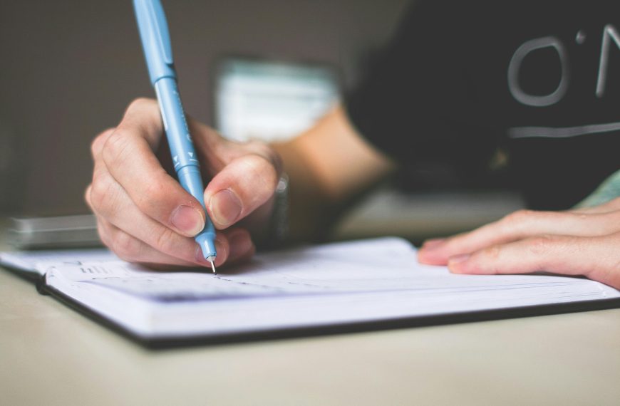 Close-up of hand writing in notebook using a blue pen, focus on creativity.